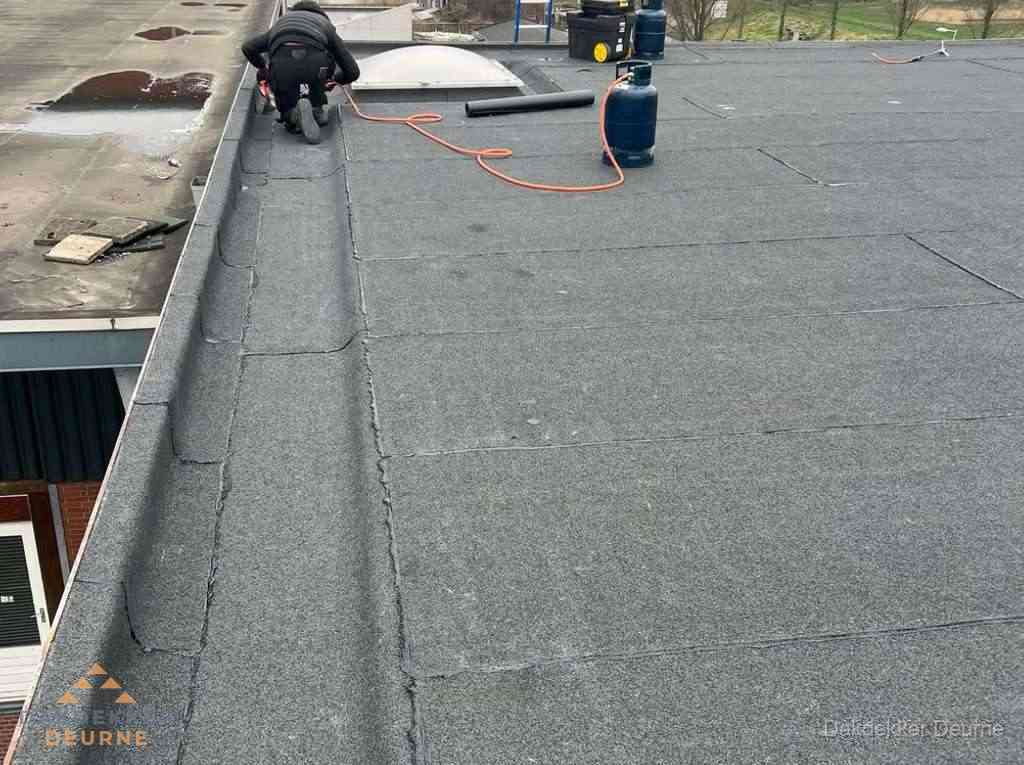 Dakdekker repareert bitumen dakbedekking op groot plat dak in Deurne